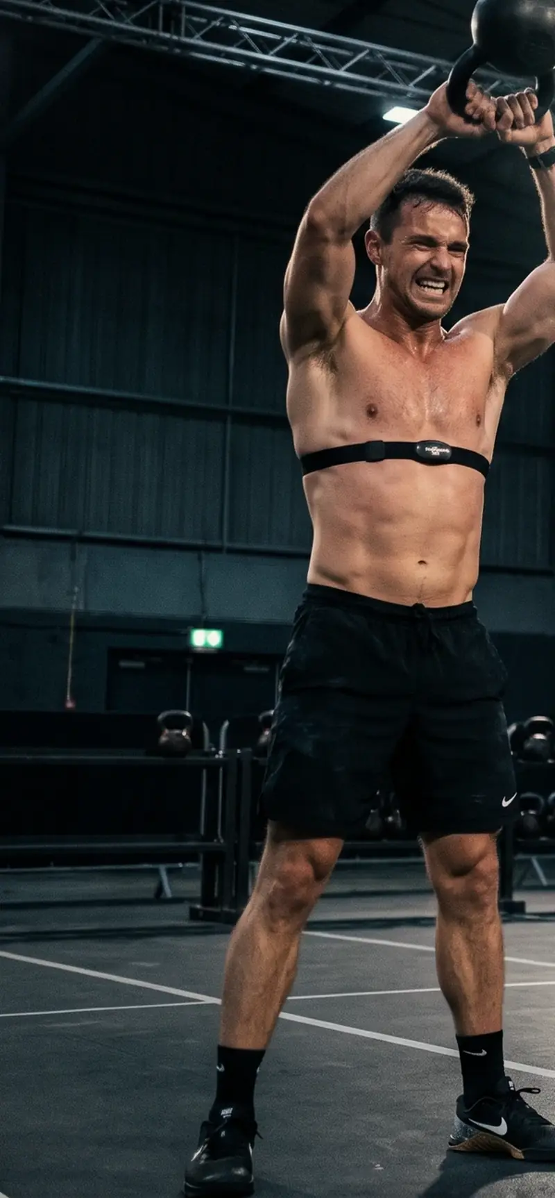An athlate user mid overhead kettlebell swing in a training hall.